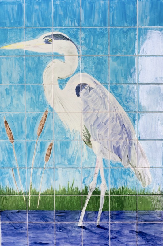 A painted mural on square tiles depicts a heron standing by water with reeds, set against a blue sky background.