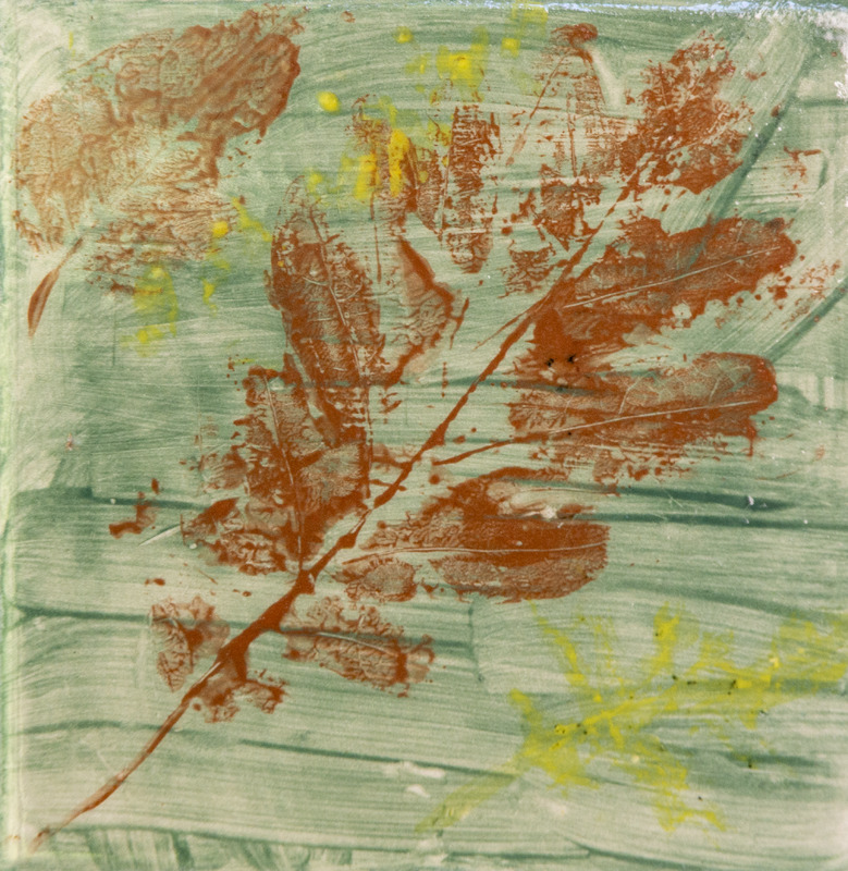 Painting of leaf print showing brown leaf impressions on a green background with small yellow paint splatters.