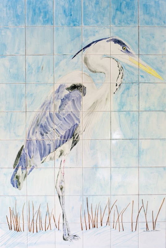 A painted mural of a heron standing in shallow water with reeds, depicted on a grid of white ceramic tiles against a blue background.